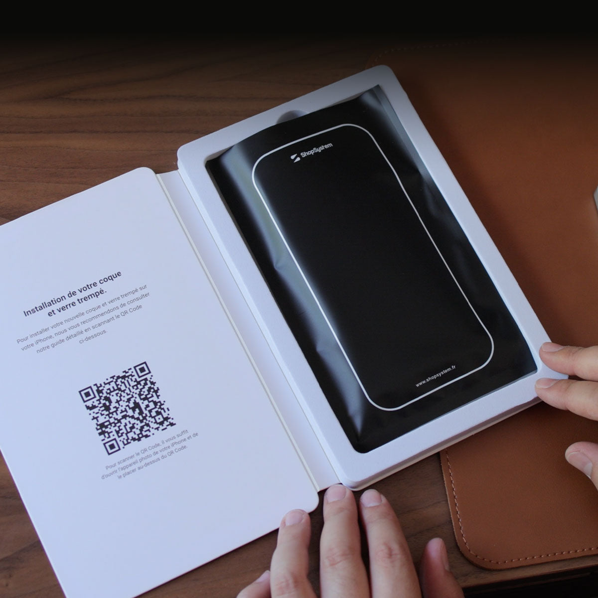 Mains ouvrant l'emballage de la coque INVISIBLE, notice d'installation et QR code visibles
