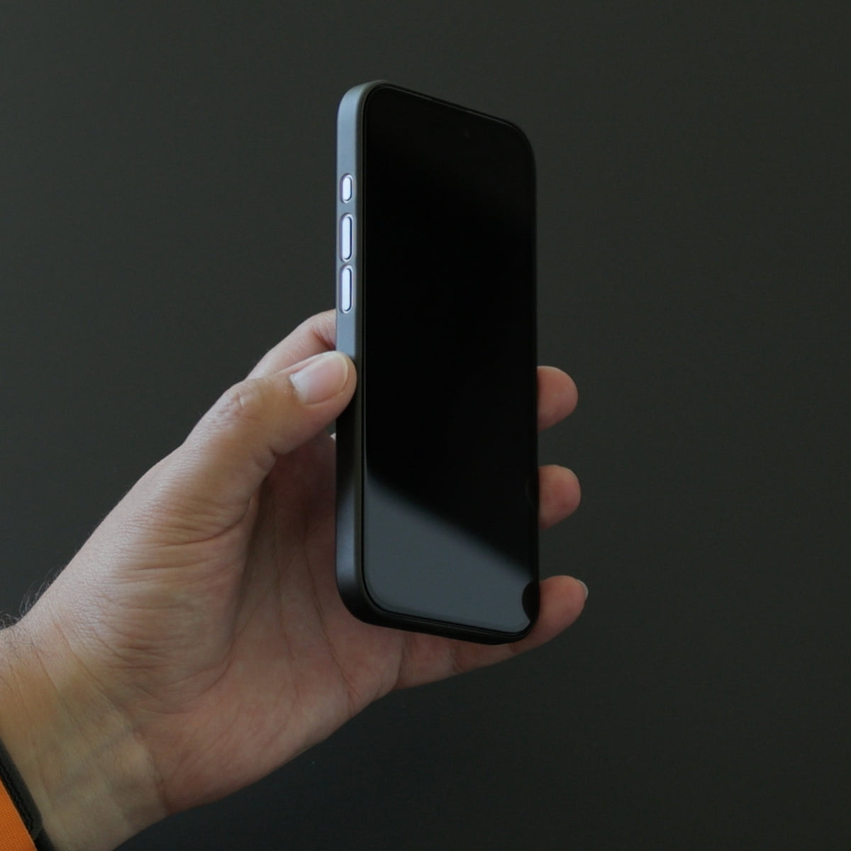 Téléphone tenu en main de profil, verre trempé posé sur l'écran éteint